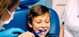 little boy brushing his teeth and smiling in the dentist’s chair