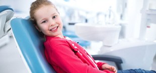 young girl smiling while sitting in dental chair 