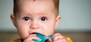 A baby chewing on a teether to help relieve discomfort