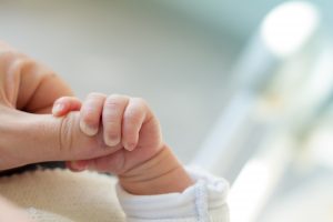 A newborn baby holding mom’s finger
