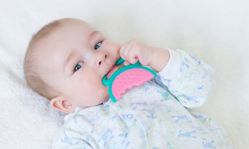 a baby lying in bed holding a teddy bear and teething in Hinsdale