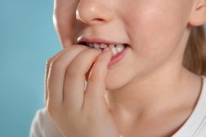 child chewing on their nails, leading to a dental emergency
