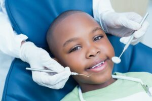 smiling child with the pediatric dentist’s hands near their face