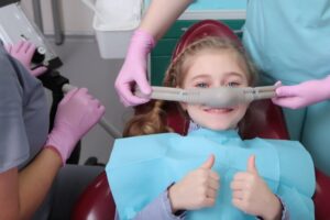 smiling little girl with two thumbs up getting sedation at her dentist’s office