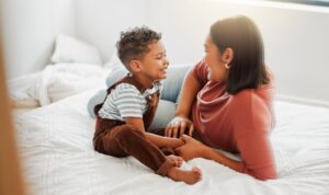 mother and toddler smiling at each other on a bed