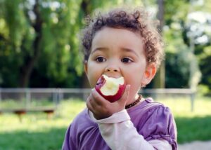 little child eating an apple outside