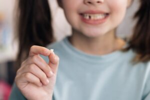 little girl smiling and holding her baby tooth