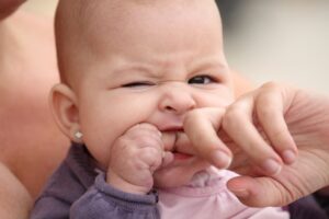 teething baby gnawing on mom’s fingers